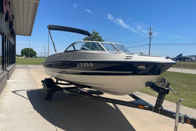 Slide: The Image of 2015 Bayliner 185 Bowrider boat on trailer, parked outdoors under clear blue sky. - 2