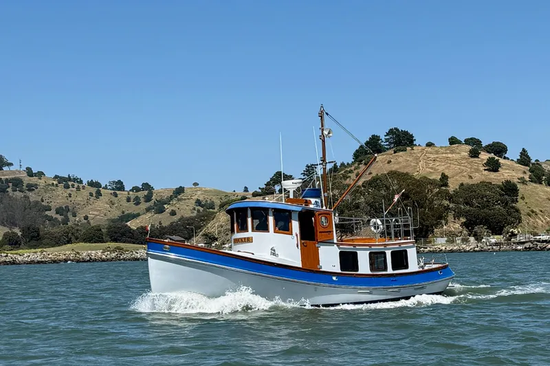 The Image of 1987 Lord Nelson Victory Tug cruising on scenic waterway with hills in background. - 0