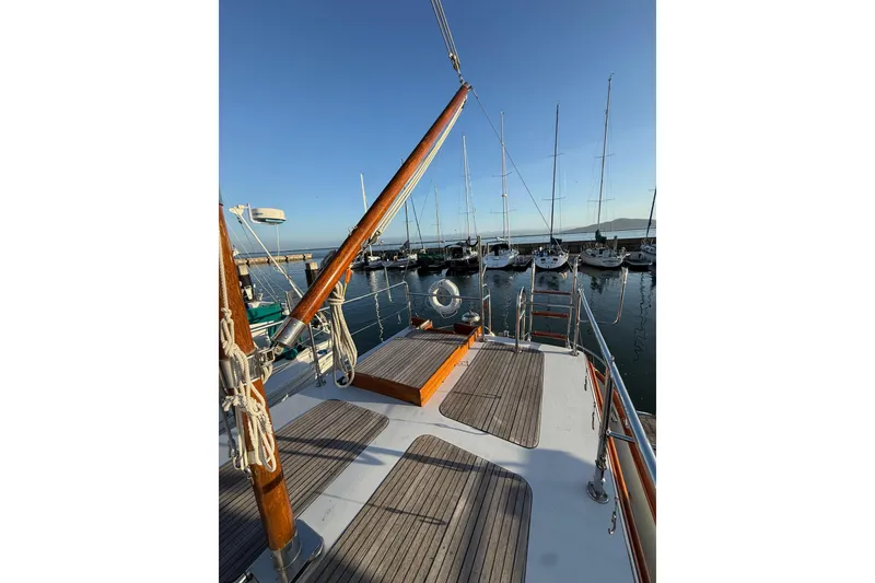 Slide: The Image of 1987 Lord Nelson Victory Tug docked at marina, wooden deck, clear sky, sailboats in background. - 14