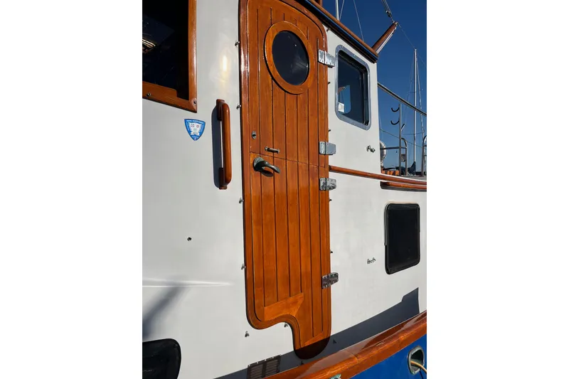 Slide: The Image of 1987 Lord Nelson Victory Tug with wooden door and porthole, docked under clear sky. - 7