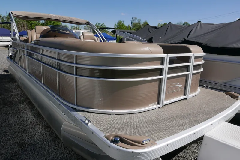Slide: The Image of 2016 Bennington 2250GSR pontoon boat with beige seating, docked on gravel under a clear sky. - 2