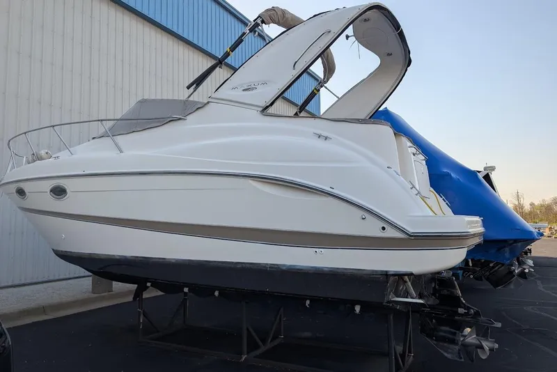 Slide: The Image of 2002 Maxum 2700 SCR boat on stands, side view, near a blue-covered vessel. - 46