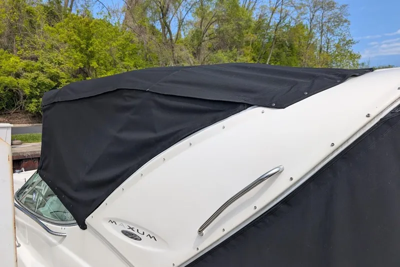 Slide: The Image of 2002 Maxum 2700 SCR boat with black cover, parked near lush greenery. - 7