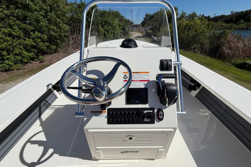 Slide: The Image of 2026 Hewes Redfisher 21 boat console with steering wheel and controls, surrounded by greenery. - 12