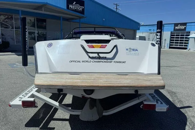 Slide: The Image of 1995 Correct Craft Ski Nautique boat, rear view, at a dealership with blue buildings. - 8