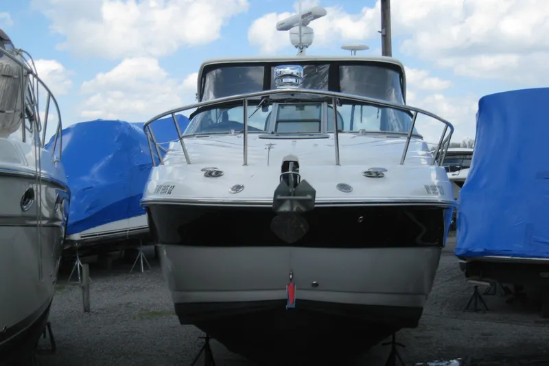 Slide: The Image of 2010 Crownline 330 CR boat docked, front view, with blue tarp-covered boats nearby. - 2