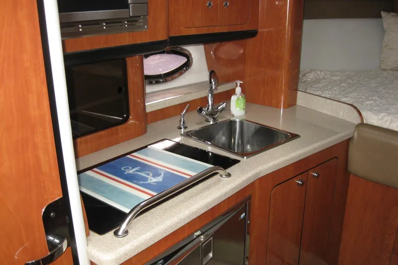 Slide: The Image of 2010 Crownline 330 CR yacht interior with kitchenette, featuring wood cabinetry and stainless steel sink. - 29