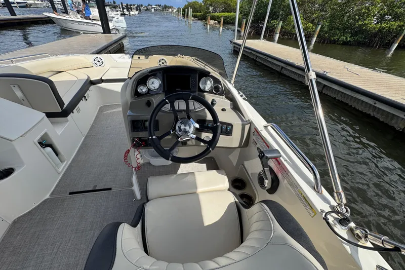 Slide: The Image of 2022 Stingray 192 SC boat interior with steering wheel, dashboard, and seating at a marina. - 11