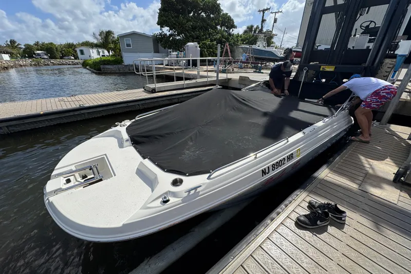 Slide: The Image of 2022 Stingray 192 SC boat docked, covered with tarp, at marina with two people working. - 38
