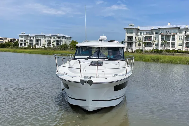 Slide: The Image of 2024 Jeanneau NC 1095 boat on calm water with buildings in the background. - 2