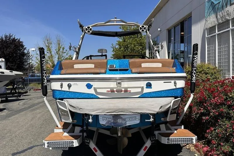 Slide: The Image of 2019 Malibu Wakesetter 25 LSV boat, blue and white, parked outdoors near a building. - 2
