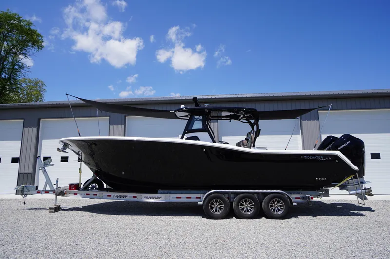 Slide: The Image of 2024 Tidewater 320 CC Adventure boat on trailer, parked outside a garage under a clear blue sky. - 64