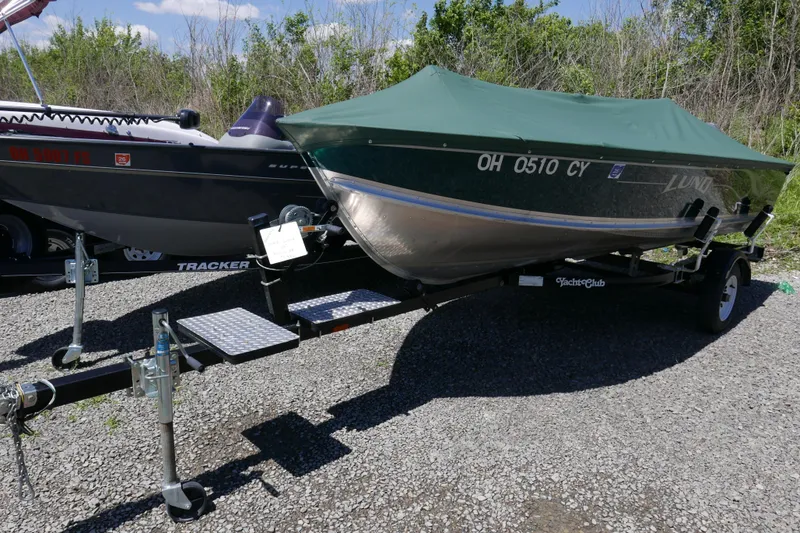 Slide: The Image of 2002 Lund 1440-V Rebel Tiller boat on trailer with green cover, parked outdoors. - 5