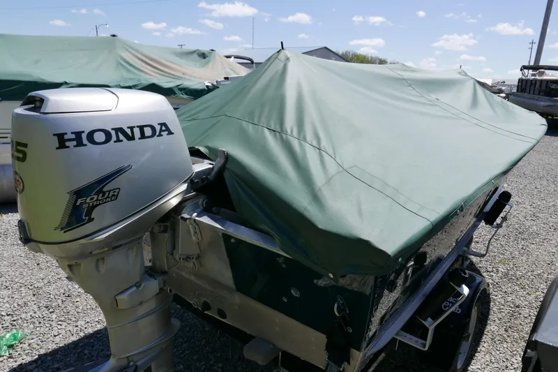 Slide: The Image of 2002 Lund 1440-V Rebel Tiller boat with Honda 15HP outboard motor, covered and parked outdoors. - 8