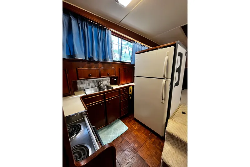 Slide: The Image of 1988 Chris Craft Constellation kitchen with wood cabinets, blue curtains, and white appliances. - 18