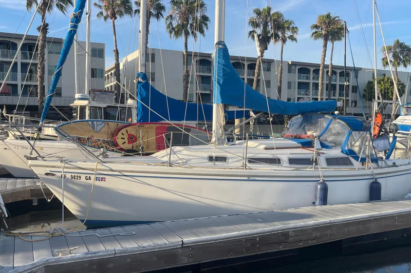 The Image of 1977 Catalina sailboat docked at marina with surfboards and palm trees in background. - 1