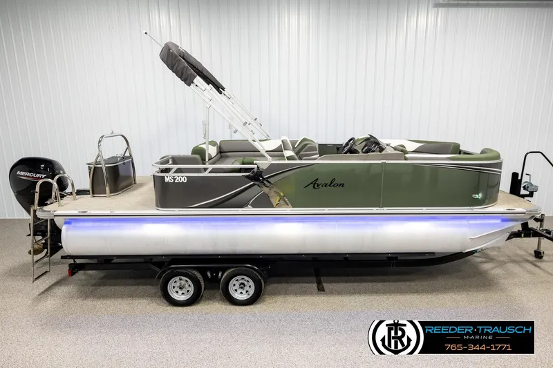 The Image of 2024 Avalon LSZ CRB pontoon boat with Mercury engine, displayed indoors on a trailer. - 1