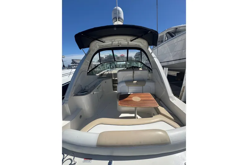Slide: The Image of 2010 Searay 330 Sundancer boat interior with seating and table, docked under clear blue sky. - 6
