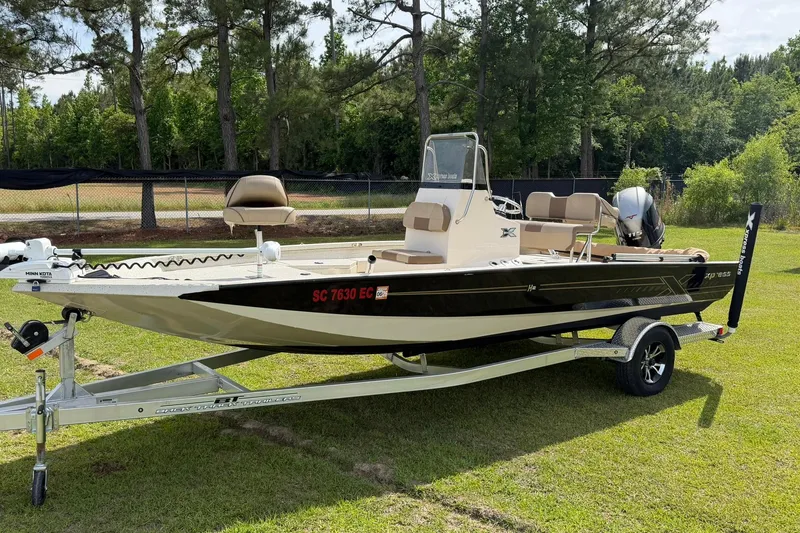 The Image of 2023 Xpress H20B Bay boat on trailer, parked on grass with trees in background. - 0