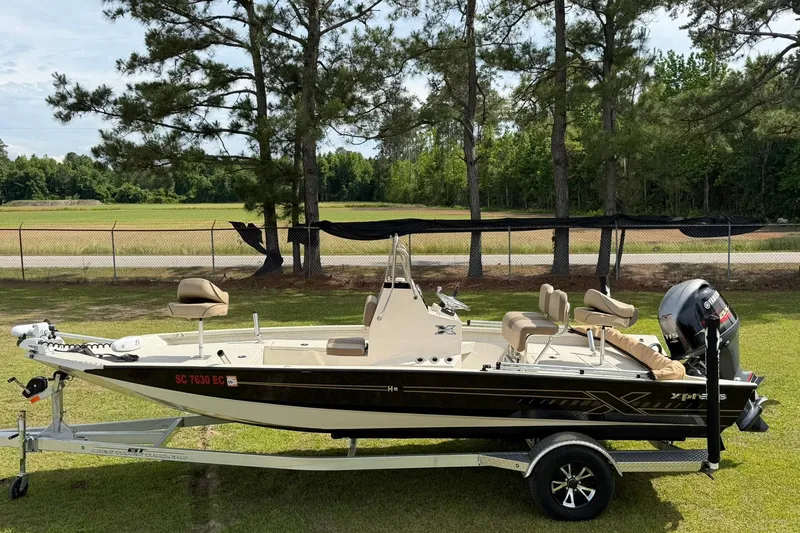 Slide: The Image of 2023 Xpress H20B Bay boat on trailer, parked on grass with trees in background. - 2