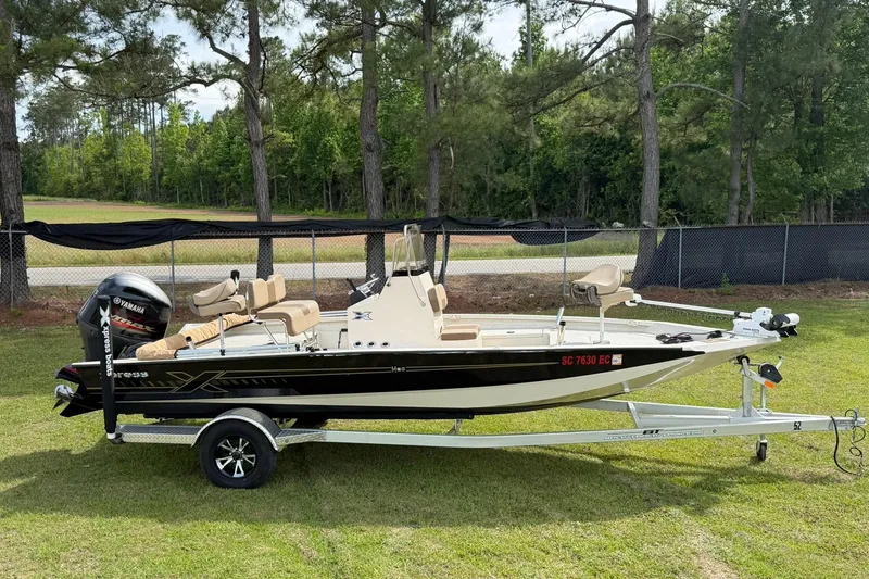 Slide: The Image of 2023 Xpress H20B Bay boat on trailer, parked on grass with trees in background. - 6