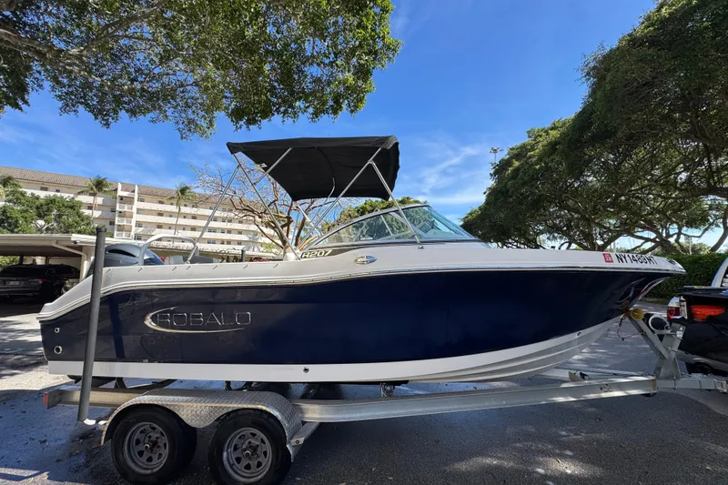 The Image of 2022 Robalo R207 Dual Console boat on trailer, parked under trees, clear blue sky. - 0