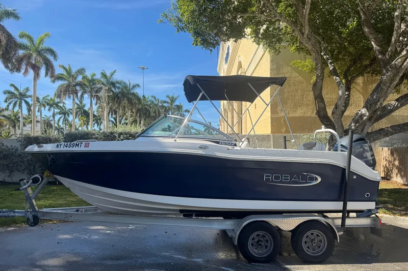 Slide: The Image of 2022 Robalo R207 Dual Console boat on trailer, parked near palm trees. - 2