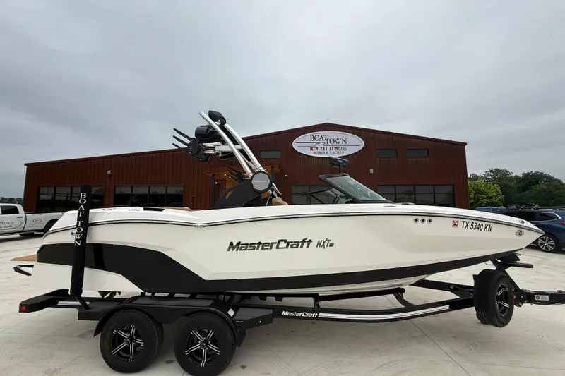 The Image of 2022 MasterCraft NXT22 boat on trailer outside dealership, overcast sky. - 1