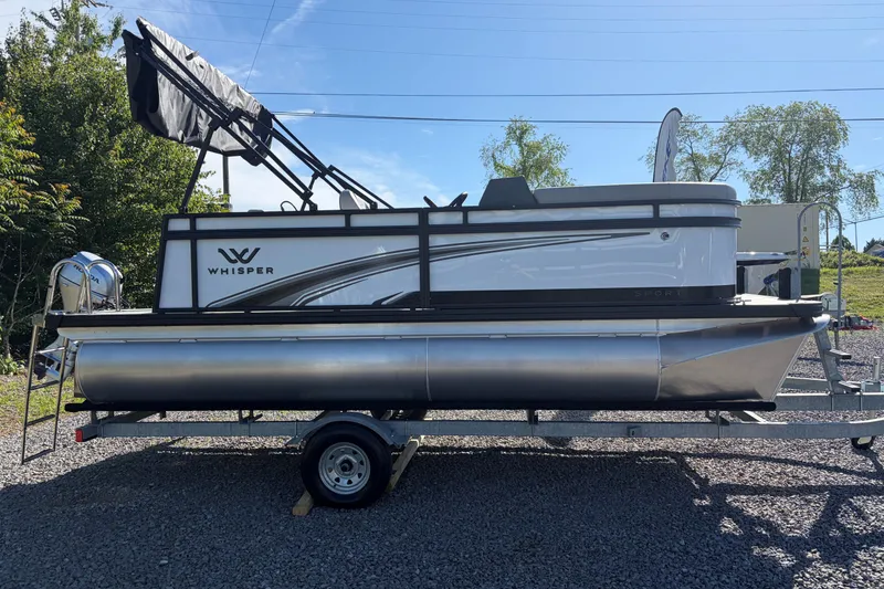 The Image of 2026 Whisper S17 pontoon boat on trailer, parked outdoors under clear blue sky. - 0
