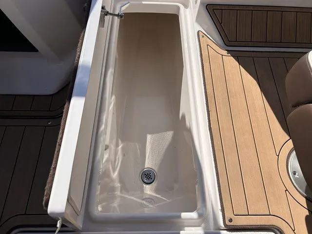 Slide: The Image of Yamaha Boats 275SE 2021 storage compartment with drain on wooden deck. - 47