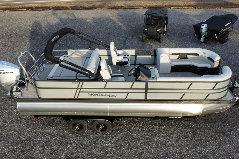 Slide: The Image of 2026 Montego Bay ST8524 SB DLX pontoon boat with Honda engine, parked on gravel. - 3