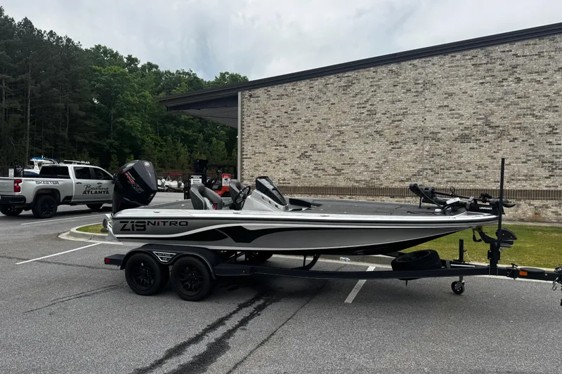 The Image of 2023 Nitro Z19 boat on trailer in parking lot, surrounded by trees and buildings. - 0