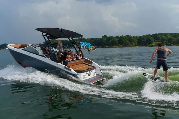 Slide: The Image of Manufacturer Provided Image: 2025 Cobalt R4 Surf boat with wakeboarder, cruising on a lake under a cloudy sky. - 2
