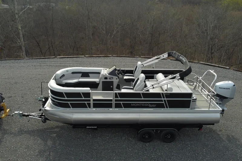 The Image of 2026 Montego Bay 140HP pontoon boat on trailer, parked on gravel surface. - 1