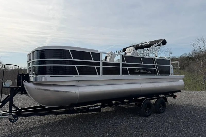 Slide: The Image of 2026 Montego Bay 140HP pontoon boat on trailer, parked outdoors. - 6