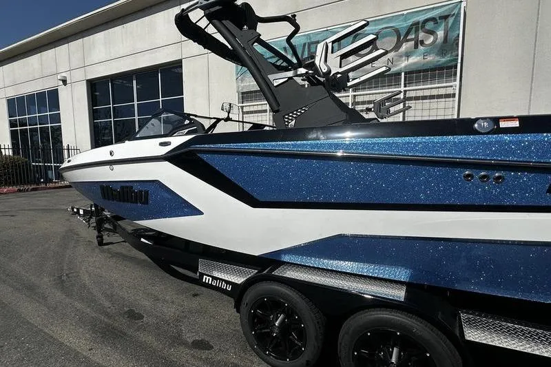 Slide: The Image of 2025 Malibu Wakesetter 23 MXZ boat with blue and white design, parked outside a building. - 2