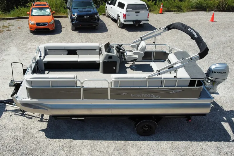 Slide: The Image of 2025 Montego Bay 90HP C8520 STD Cruise Pontoon on trailer, parked near vehicles. - 2