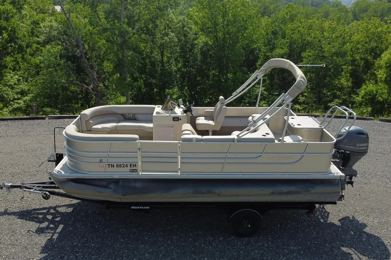 The Image of 2015 Starcraft Stardeck 216 Cruise-N-Fish pontoon boat on trailer, surrounded by lush greenery. - 0
