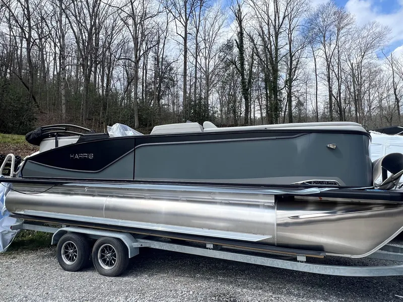 The Image of 2026 Harris Sunliner 230 pontoon boat on trailer in wooded area. - 1