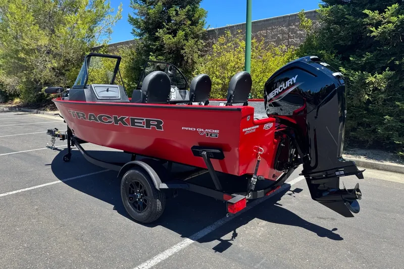 Slide: The Image of Red 2026 Tracker Pro Guide V-16 WT boat with Mercury outboard motor in parking lot. - 2