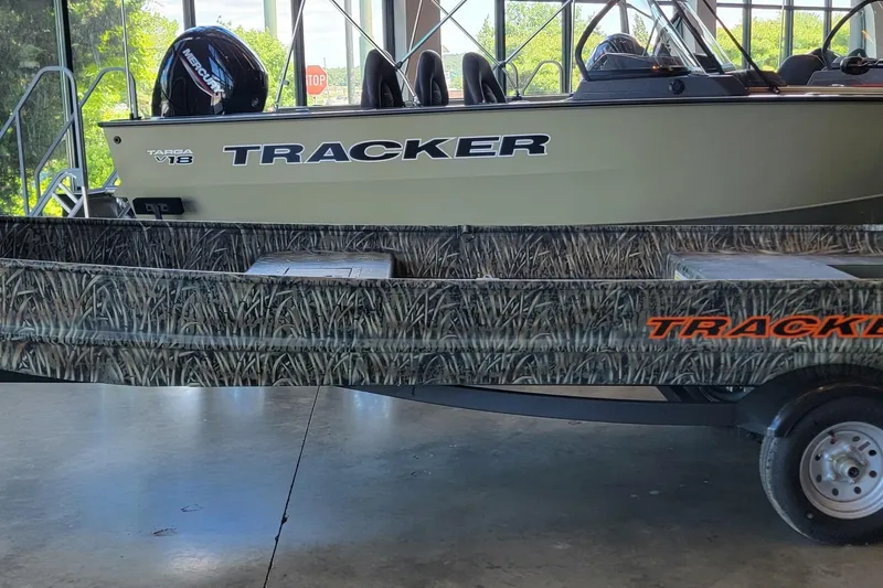 The Image of 2026 Tracker Grizzly 15 Jon boat with camo design on trailer in showroom. - 0