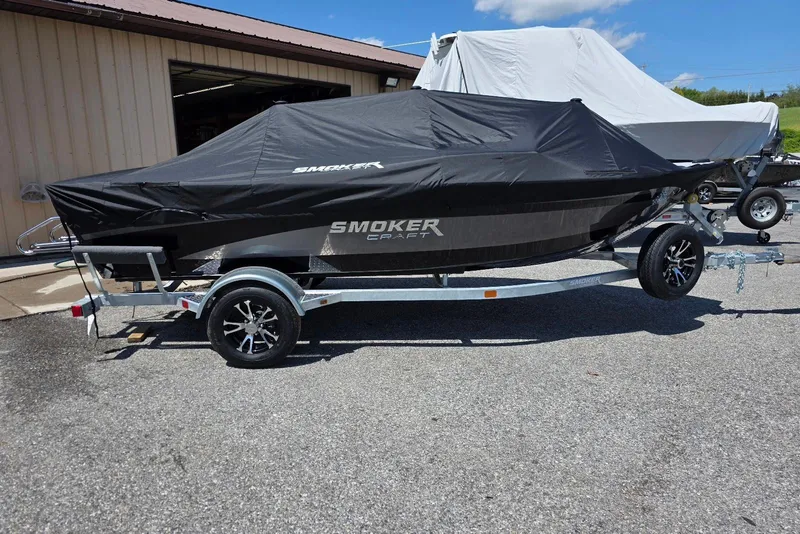 Slide: The Image of 2026 Smoker Craft Pro Angler 165 SC boat covered on a trailer, parked outdoors. - 2