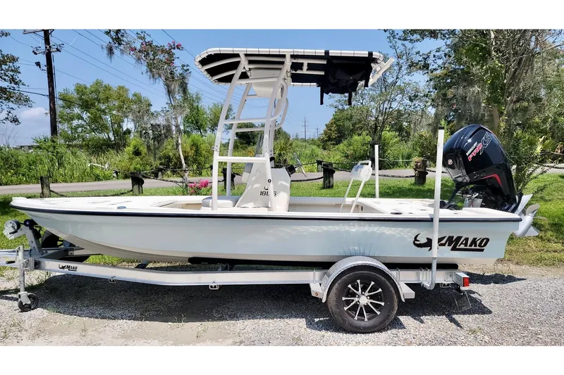 The Image of 2023 Mako 18 LTS boat on trailer, parked outdoors with lush greenery background. - 0