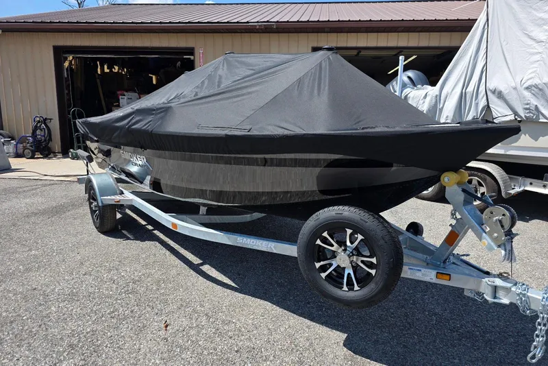 Slide: The Image of 2026 Smoker Craft Pro Angler 165 SC boat covered on trailer, parked outside a garage. - 3
