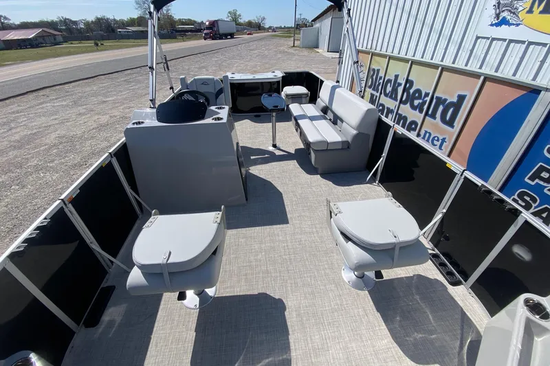 Slide: The Image of 2026 SunCatcher Select 18F pontoon boat interior with seating and helm, parked near a road. - 7