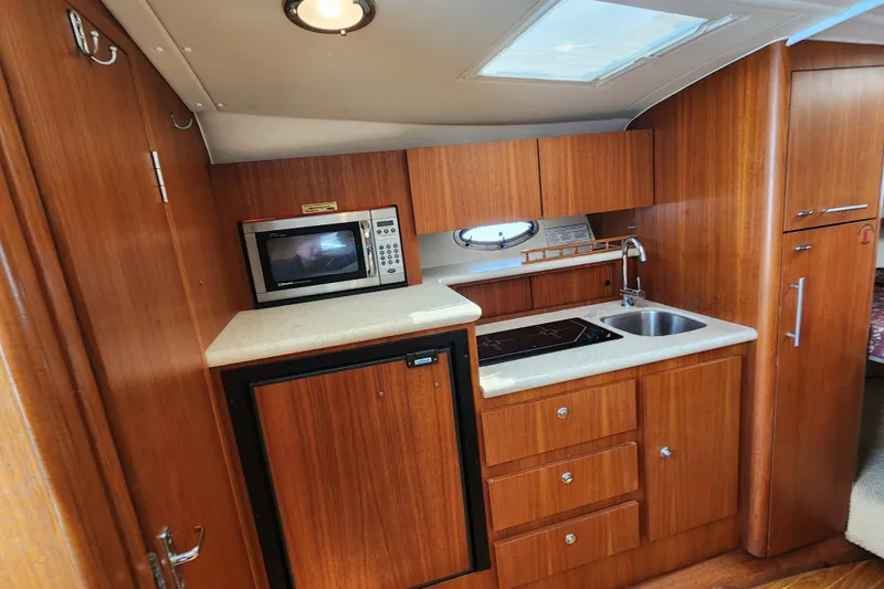 Slide: The Image of 2003 Tiara Yachts 3100 Open LE galley with microwave, sink, and wooden cabinetry. - 35
