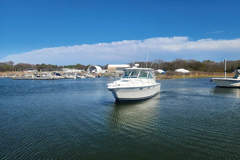 Slide: The Image of 2003 Tiara Yachts 3100 Open LE cruising near a marina under a clear blue sky. - 46