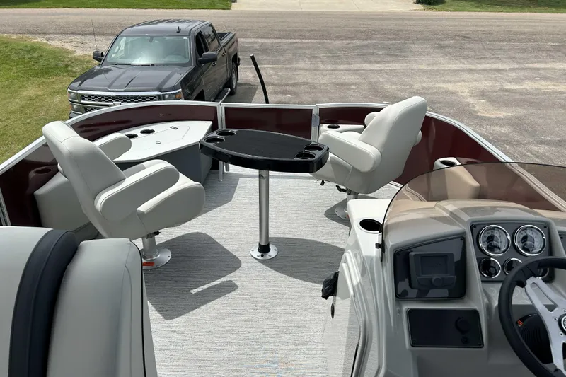 Slide: The Image of 2026 Starcraft EX 20 F pontoon boat interior with seating and table, parked truck nearby. - 4