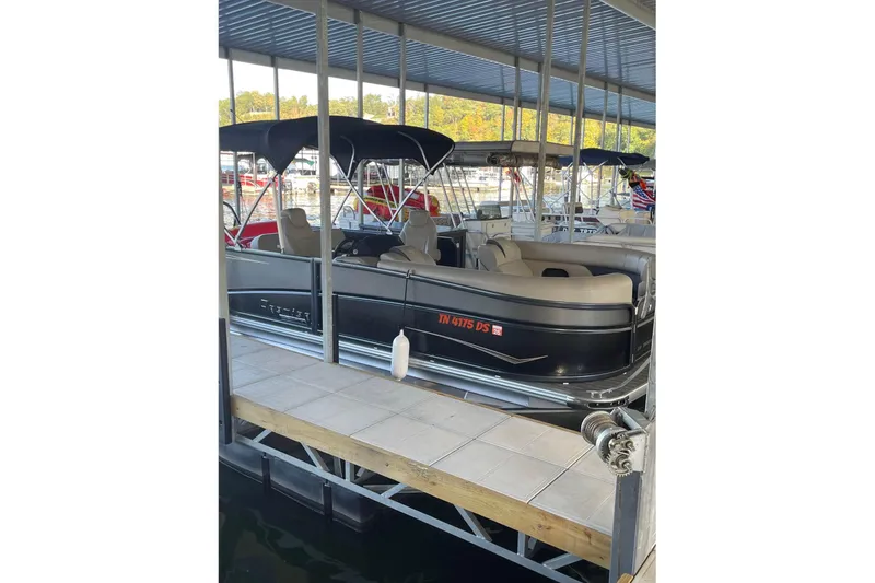 Slide: The Image of 2023 Premier Sunsation pontoon boat docked in a marina under a covered structure. - 1
