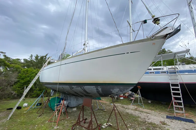 Slide: The Image of Vintage 1979 Fuji 40 sailboat on stands, under cloudy sky, surrounded by greenery. - 16